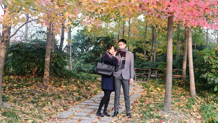 Fototapeta na wymiar Portrait of a beautiful Chinese young woman hugging her boyfriend's shoulder in autumn forest park, warm sunlight lighting their face, romantic moment.