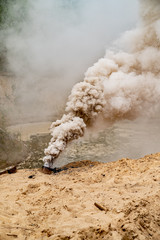 Grey smoke comes out from smoke bomb. The bomb on sand near a forest. Military training. Air...