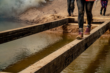 Girl crosses an obstacle at a sporting event. Only legs. Walking along a narrow beam above the water