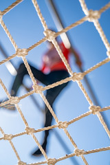 White net close-up. A blurry person overcomes an obstacle In the background. Sport event. Clear blue sky