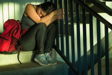 Dramatic portrait of Asian female college student bullied. Young depressed and sad Chinese girl sitting lonely on campus staircase suffering bullying and harassment feeling desperate and excluded