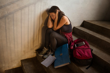Dramatic portrait of Asian female college student bullied. Young depressed and sad Japanese girl sitting lonely on campus staircase suffering bullying and harassment