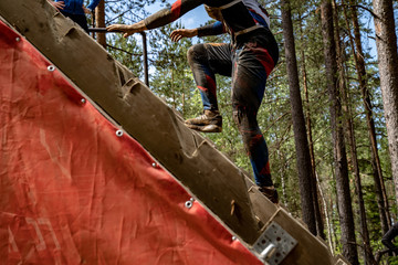 A man climbs an obstacle at a sporting event. He hard goes up on top of obstacle. Sport activity in the forest