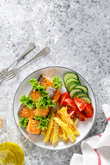 Grilled salmon kebab on skewers with baked potato, fresh cucumbers and tomatoes