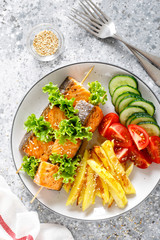 Grilled salmon kebab on skewers with baked potato, fresh cucumbers and tomatoes