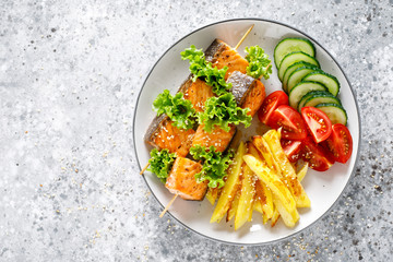 Grilled salmon kebab on skewers with baked potato, fresh cucumbers and tomatoes