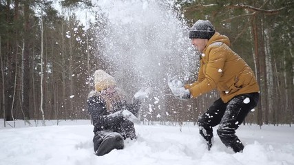 Young happy couple, man and woman, are having a fun time throwing a snow each other in winter forest in slow motion. Family weekend. - Powered by Adobe