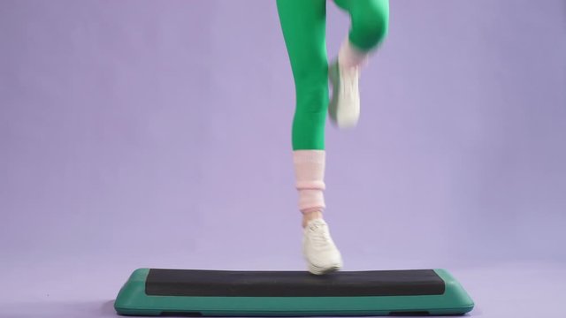 Female aerobics trainer showing how to do step ups on fitness platform in gym, trains glutes and legs, jumps actively, has beautiful body curves and muscles, full of strength and energy