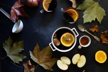 White mug with mulled wine. Autumn and winter warm alcoholic drink. Autumn leaves, honey, apples, oranges, vintage dishes. Autumn cozy mood. Flat lay, dark background.