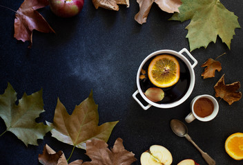 Obraz na płótnie Canvas White mug with mulled wine. Autumn and winter warm alcoholic drink. Autumn leaves, honey, apples, oranges, vintage dishes. Autumn cozy mood. Flat lay, dark background.