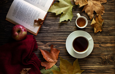A cup of hot tea, a mug with honey, autumn leaves, a book and a woolen sweater on a rustic...