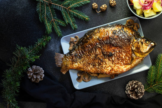 Christmas whole Carp baked with mushrooms. Served on a dark background with potato salad. Traditional Christmas Eve meal. Top view. Space for text