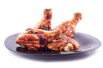 grilled chicken legs to a crust in a black plate on a white background isolated