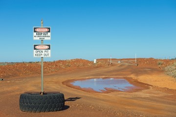 Danger Sign at Mining Site, with red sand and sunny blue background with copy space.