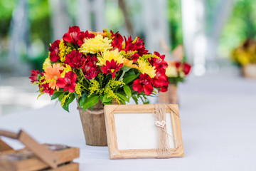 Garden wedding table set up decoration - fresh red and yellow flowers and a blank photo frame/board