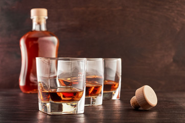 Glass of whiskey on a wooden tableThree glasses of whiskey on a wooden table, a full bottle of whiskey in the background
