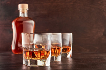 Glass of whiskey on a wooden tableThree glasses of whiskey on ice on a wooden table, a full bottle of whiskey in the background