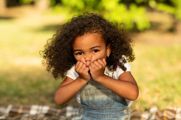 Little girl grimacing and touching cheeks in nature park - obrazy, fototapety, plakaty