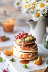 Obraz na płótnie Canvas Cornmeal pancakes with salted caramel served with berries and fruits on a white wooden background.