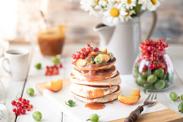 Obraz na płótnie Canvas Cornmeal pancakes with salted caramel served with berries and fruits on a white wooden background.