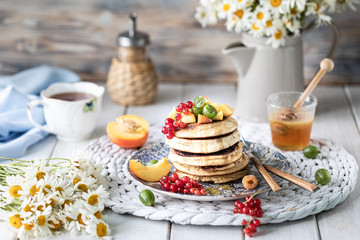 Cornmeal pancakes with honey, served with berries and fruits on a white wooden background.