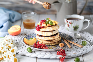 Cornmeal pancakes with honey, served with berries and fruits on a white wooden background.