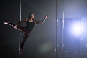 The dancer on the pylon in the studio. Girl doing exercises on a sports equipment.