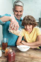 Cheerful father making breakfast for son at kitchen