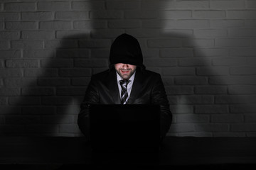 Hacker in black mask and hood at the table