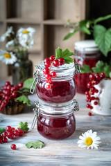 Red currant sauce or jam in two glass jars and fresh berries and flowers on a wooden background
