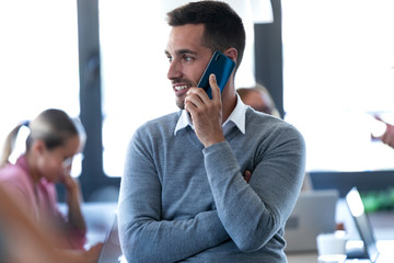 Smiling young businessman talking on mobile phone on coworking space.