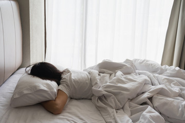 Woman stretching in bed after waking up, back view. Woman sitting near the big white window while stretching on bed after waking up with sunrise at morning, back view.