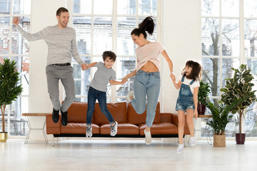 Happy active parents with kids holding hands jumping at home