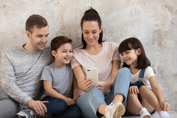 Happy parents with children sit on floor looking at phone