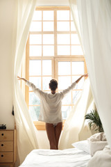 Young lady opening curtains in the morning