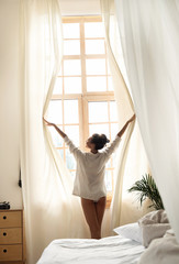 Fototapeta na wymiar Attractive lady in shirt opening curtains in the morning