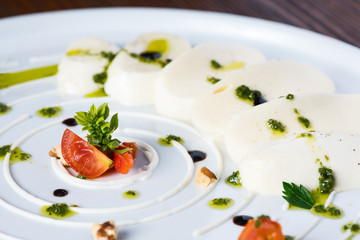 Mozzarella and tomatoes set with pesto sous with greens on white plate close up