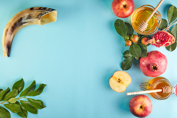 Rosh hashanah - jewish New Year holiday concept. Traditional symbols: Honey jar and fresh apples with pomegranate and shofar -horn on a blue background. Copy space for text.