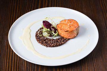 Grilled salmon fish with kinua, decorated with greens and salad on white plate