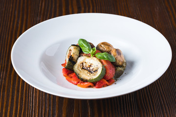 Grilled vegetables, tomatoes, cabbages, zukini, decorated with basil on white plate