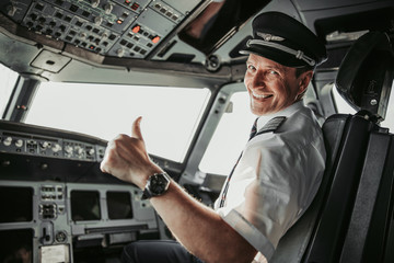 Smiling pilot in cockpit looking at camera - obrazy, fototapety, plakaty