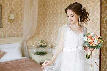 Fototapeta na wymiar Pretty young Bride.Brown-haired woman with classic wedding hair-style. Boudoir morning of the bride. Taking wedding bouquet in her hands