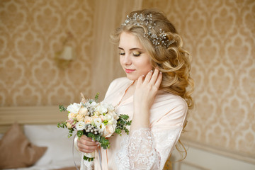 Pretty young girl. Blonde woman with luxurious long curly hair. Boudoir morning of the bride. Taking wedding bouquet in her hands. Touching her neck