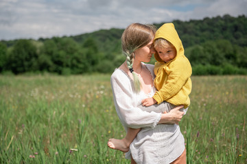 mom holds in her arms a little son in yellow clothes in a meadow