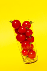Fototapeta na wymiar Red cherry tomatoes in the glass over yellow background. Colorful food background. Advertising, food, smoothies concept.
