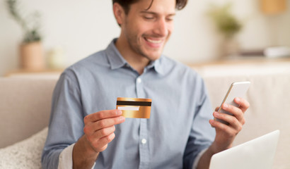 Guy holding credit card and using mobile phone at home