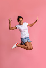 Positive african american girl jumping over pink studio background