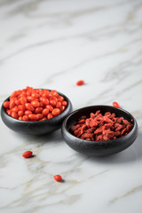 Frische und getrocknete Goji-Beeren Superfood in schwarzer Porzellan Schale auf Marmor Hintergrund