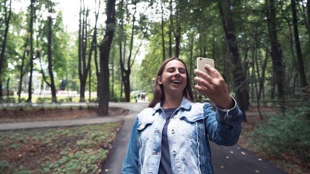 Young beautiful woman calling by phome in Jean jacketwalking in summer park. video calling