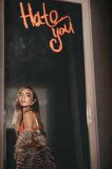 Obraz premium Seductive woman portrait of trendy woman in fur coat and lingerie. Inscription hate you. Stylish fashion girl model posing in mirror in room